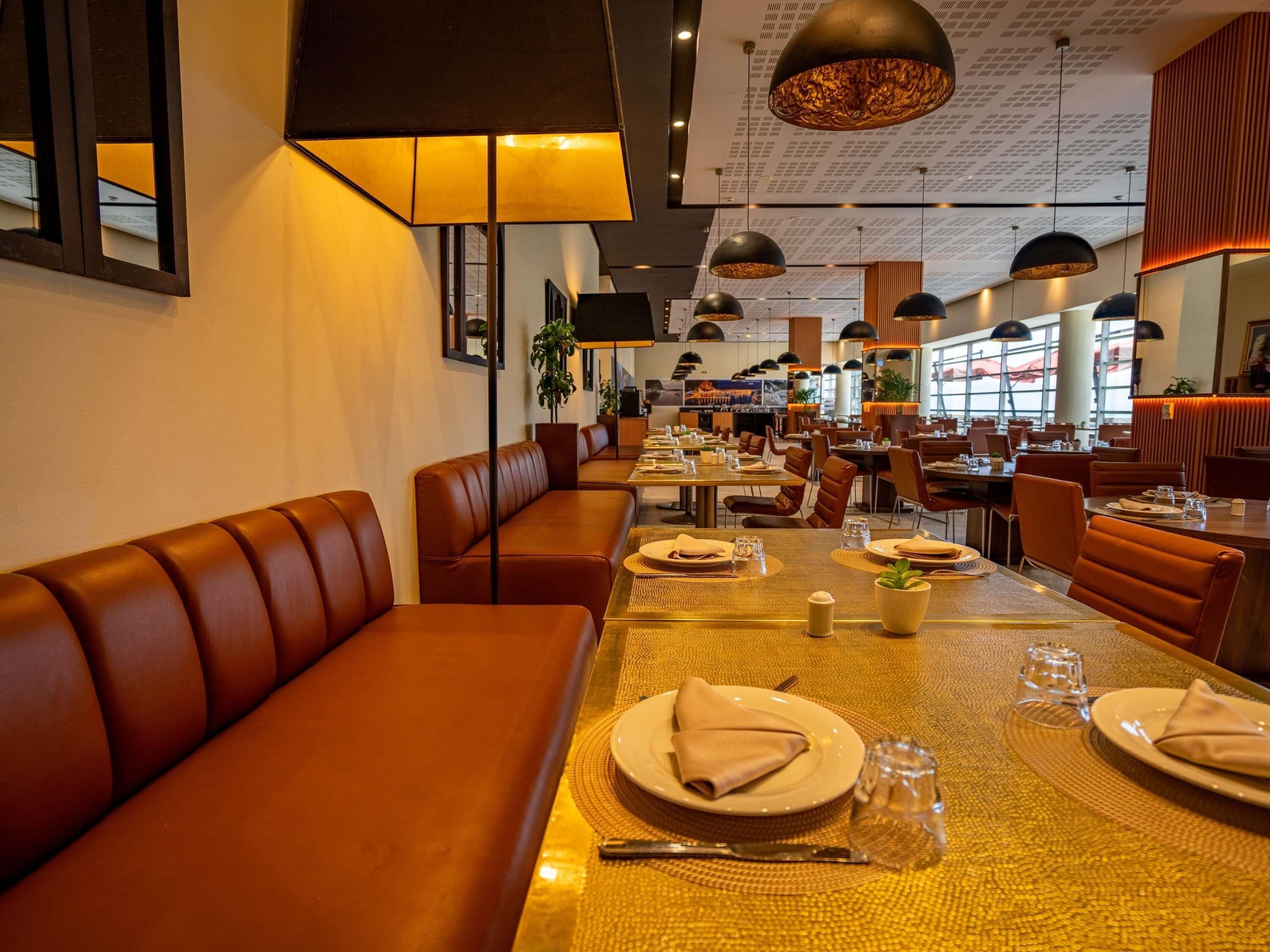 A restaurant with leather booths, round tables, and pendant lighting.