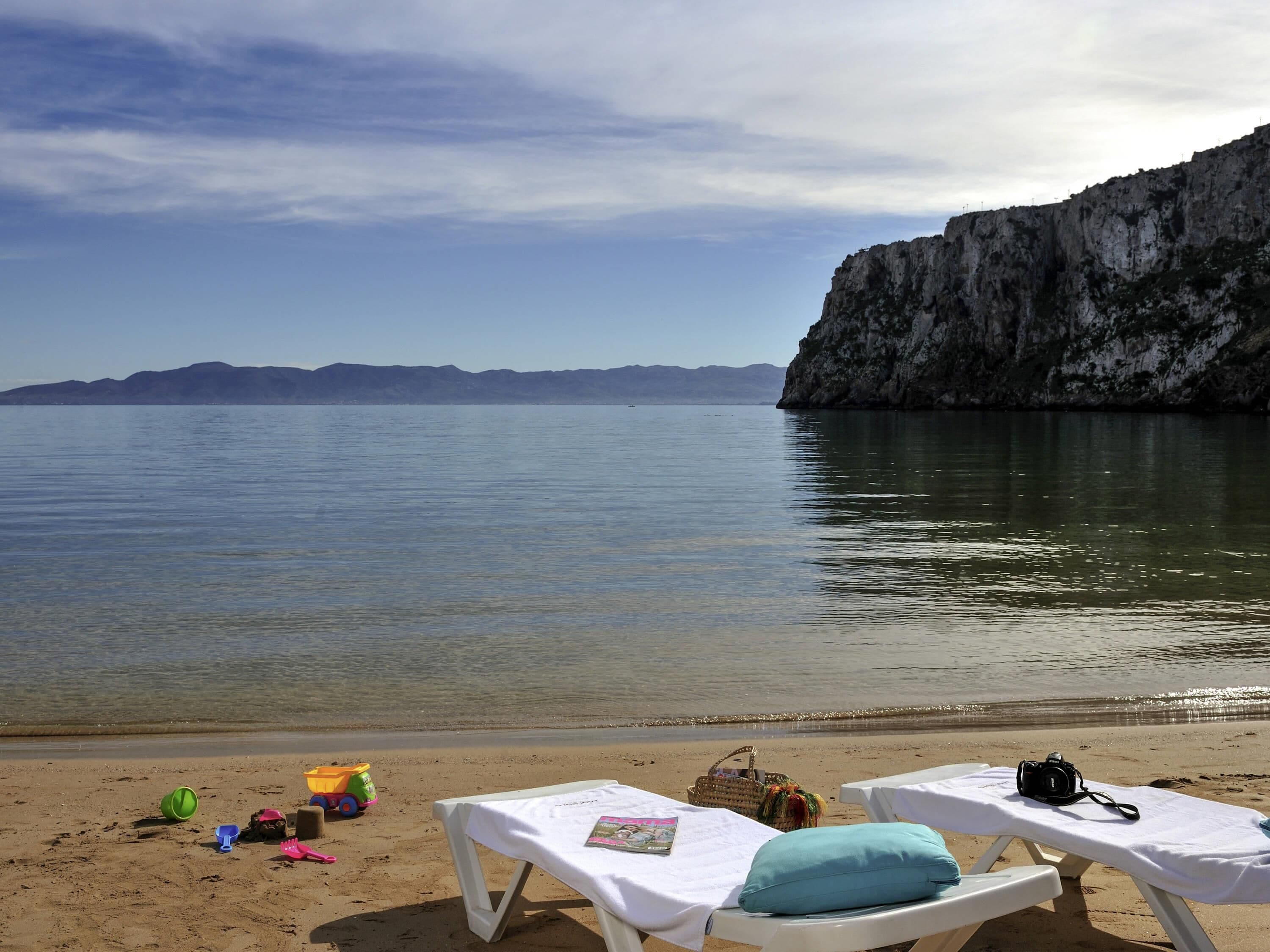 A beach with lounge chairs, a beach ball, a toy truck, and a camera on the sand.