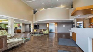 A spacious lobby with a curved reception desk, seating area with patterned sofas, and a kitchen in the background. - Best Western Plus Patterson Park Inn (Arkansas City)