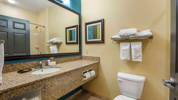 A bathroom with a granite countertop sink, a toilet, a towel rack with towels, and framed artwork on the wall.