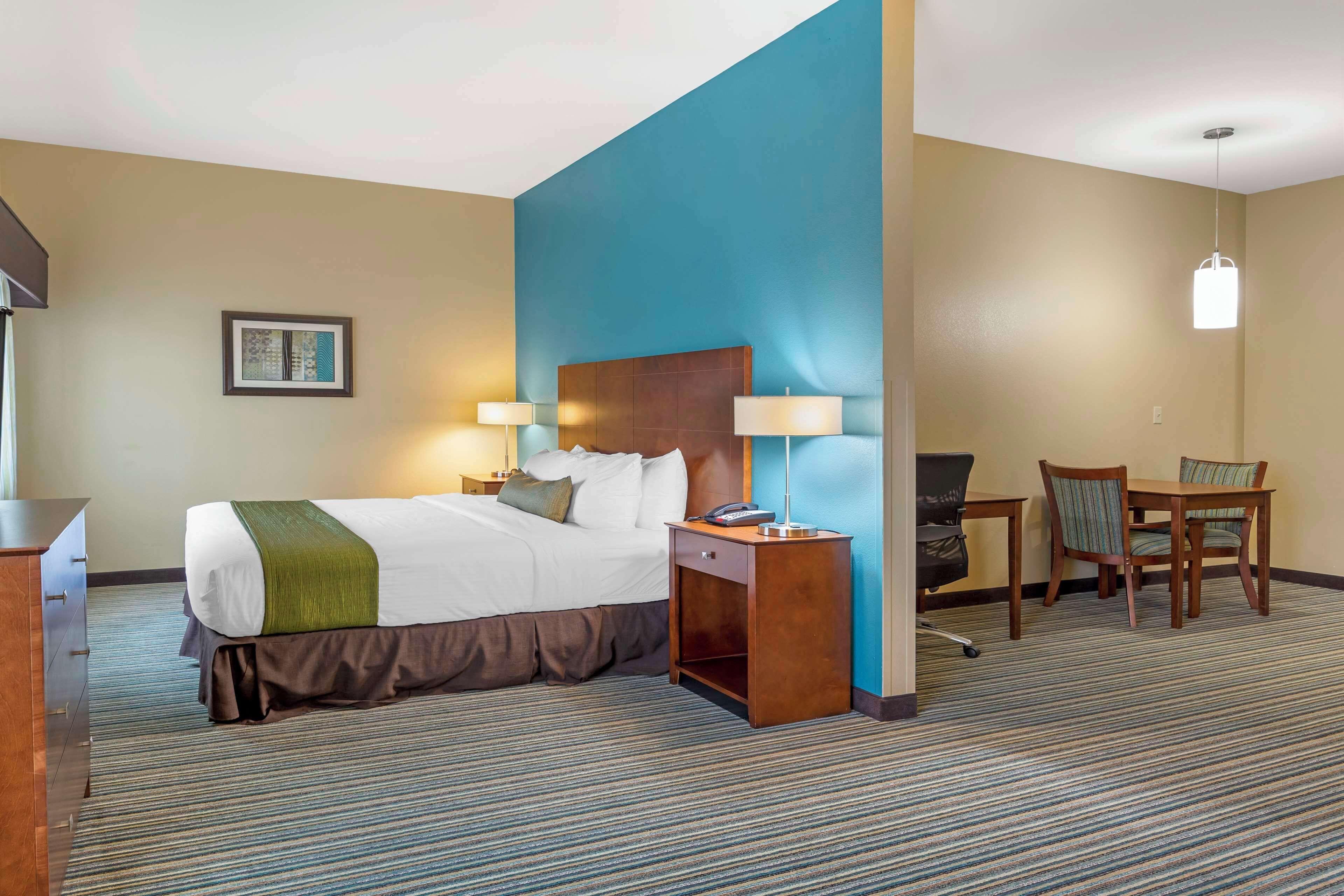 A hotel room with a large bed, bedside tables with lamps, a desk with a chair, and a blue accent wall.