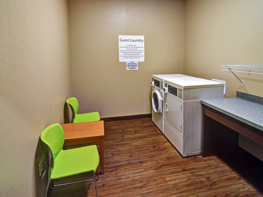 A small laundry area with a washing machine, a drying rack, and two green chairs.