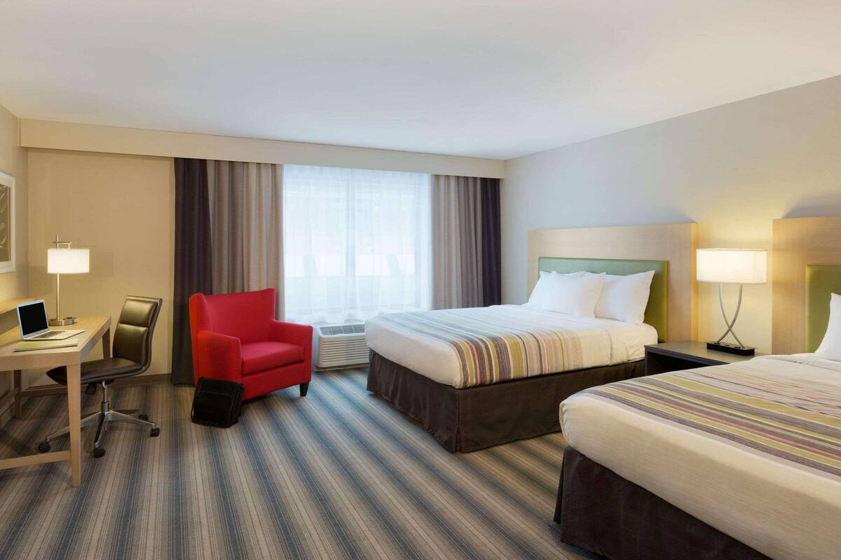 Habitación de hotel con cama, escritorio, silla y ventana con cortinas.