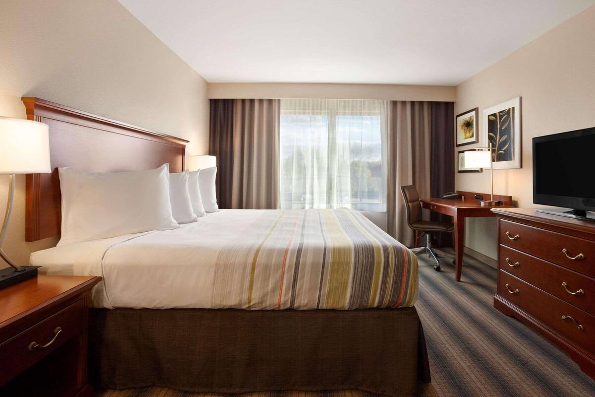 Habitación de hotel con una cama grande, un escritorio, televisión y vista al exterior a través de la ventana.