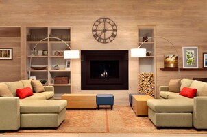 A modern living room with two sofas, a coffee table, and a fireplace. There are shelves with decorative items and a clock on the wall.