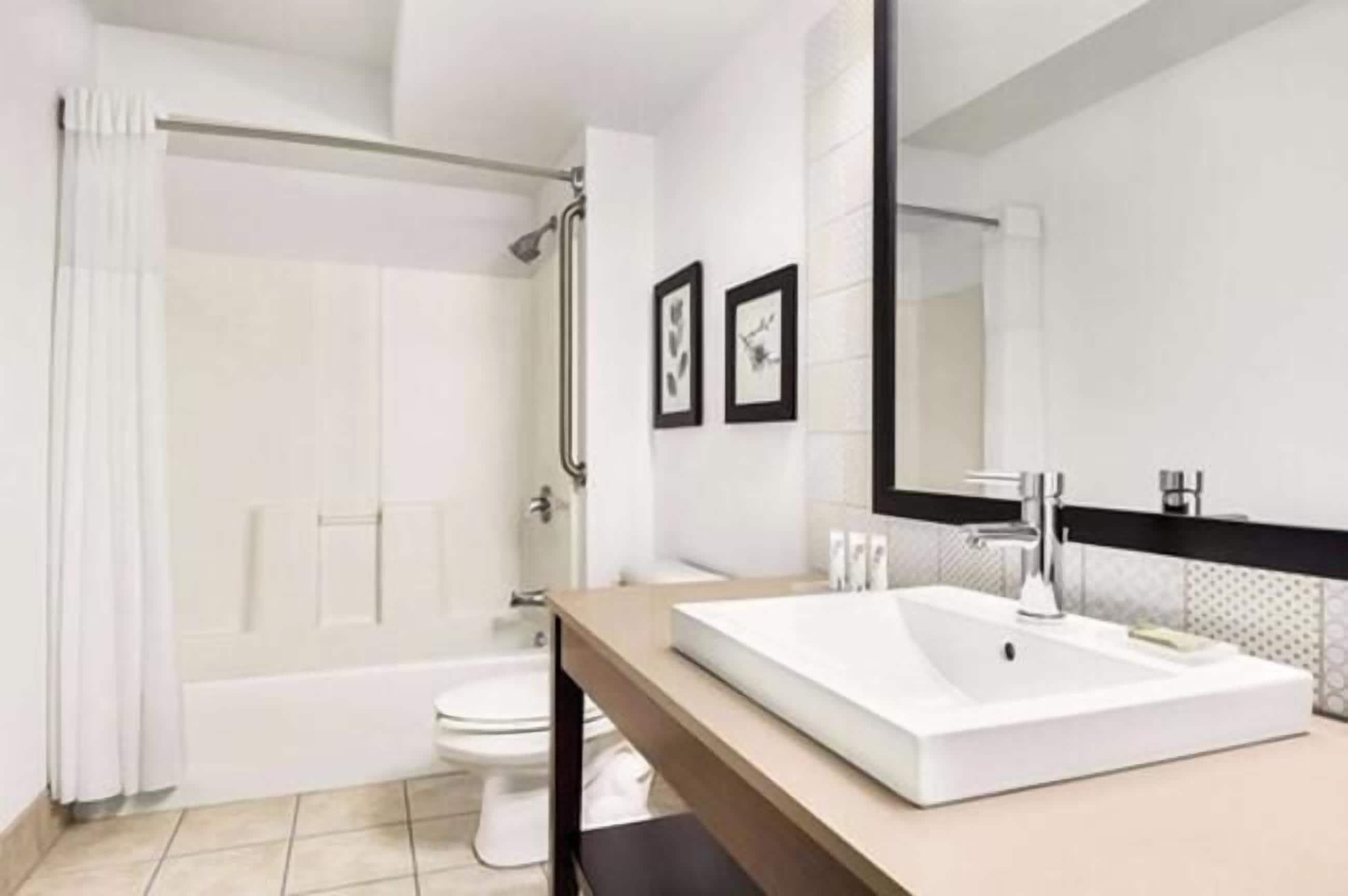 A modern bathroom with a bathtub, toilet, and a large mirror above a sink.