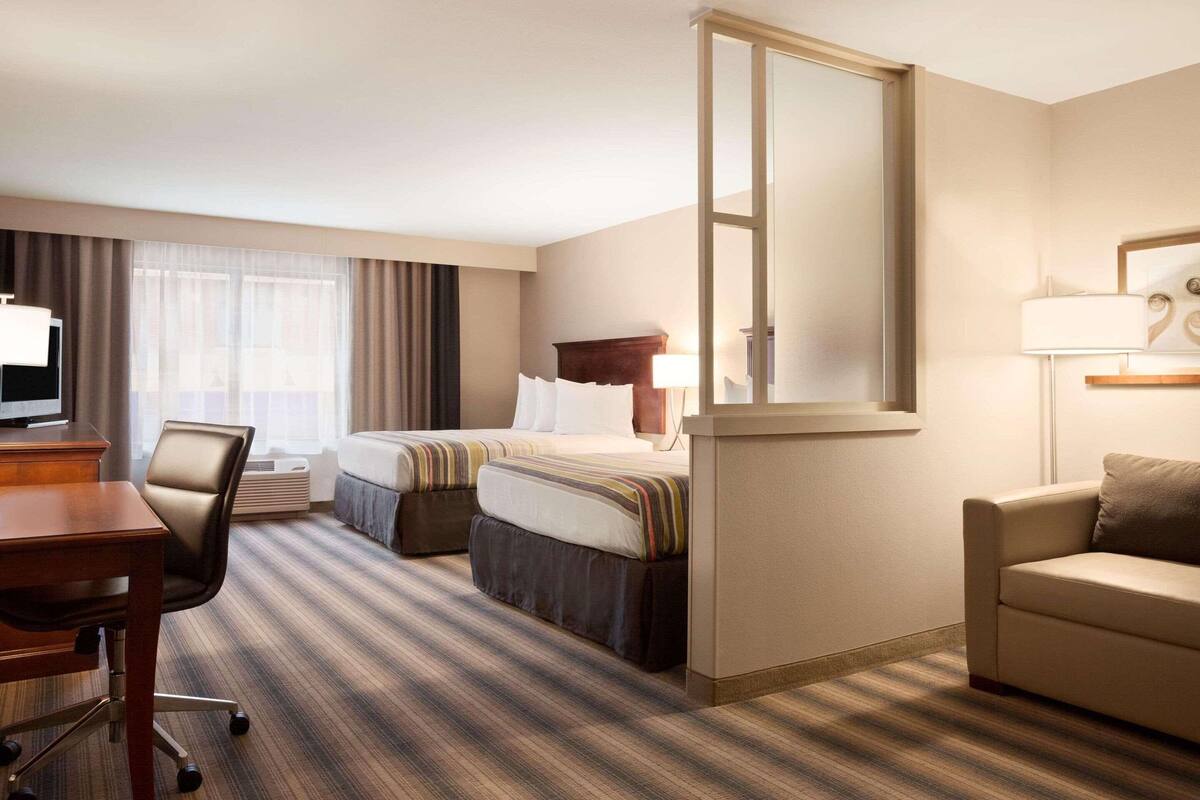 Habitación de hotel con cama, escritorio, silla, sofá, televisión y ventana con cortinas.