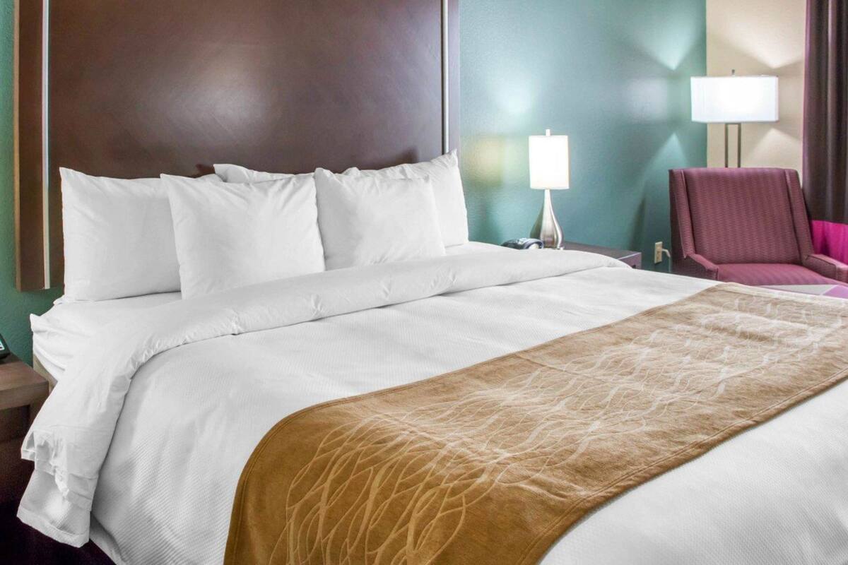 Ett hotellrum med en stor säng, ett nattduksbord med en lampa och en stol.