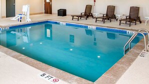 Piscina interior com espreguiçadeiras e mesas, marcações de profundidade e sinal de saída.