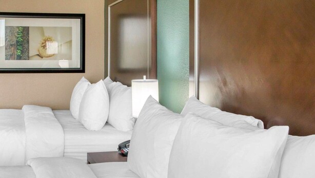 Quarto de hotel com uma cama grande, um sofá menor, uma mesa de cabeceira com abajur e um quadro na parede.