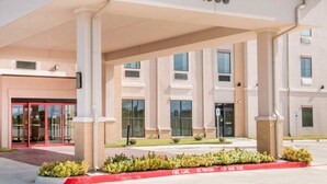 Entrada moderna de hotel com galeria coberta, número 1053, e placa vermelha indicando 'Proibido Estacionar'.