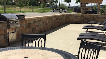 An outdoor patio with a stone wall, a grill, and lounge chairs.