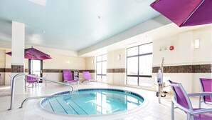Une piscine intérieure dotée d’un sol carrelé, de fauteuils de couleur violette et d’un plafond pourvu d’un éclairage encastré.
