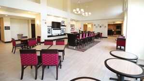 A spacious dining area with multiple tables and chairs, a kitchen in the background, and a modern chandelier.