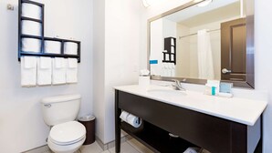 A modern bathroom with a white toilet, a black vanity with a mirror, and a towel rack with multiple towels.