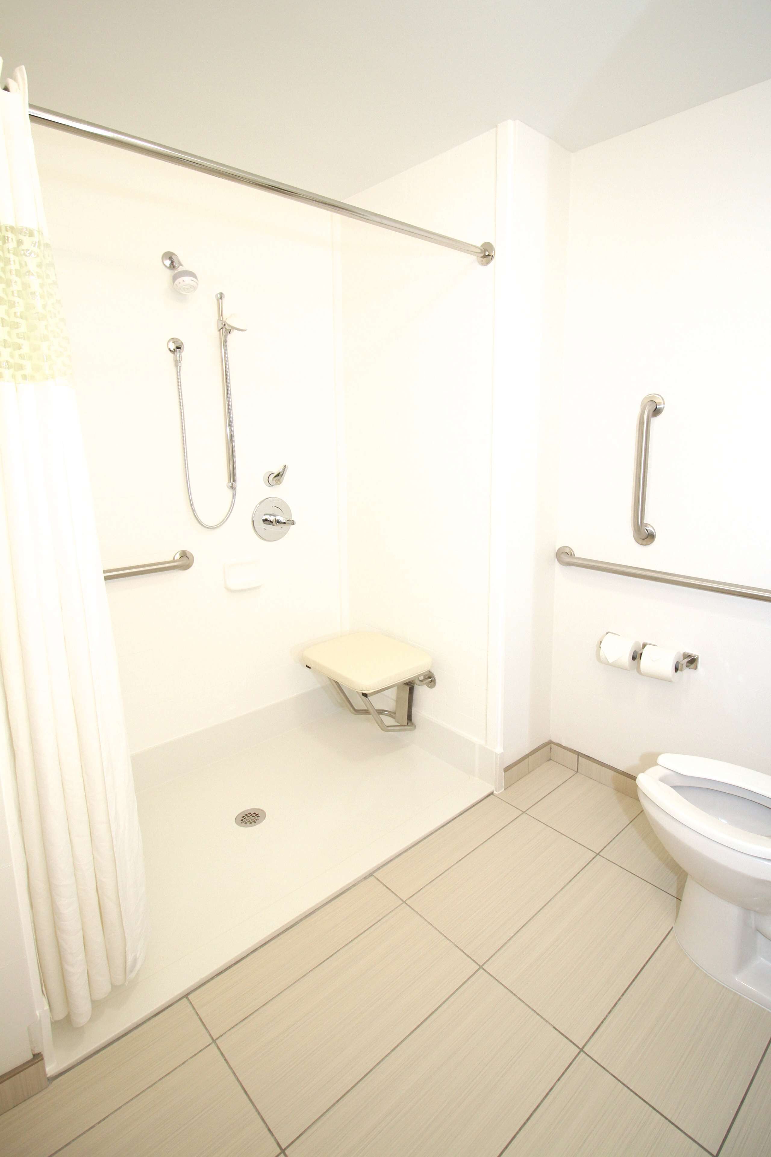 A bathroom with a shower, toilet, and grab bars.