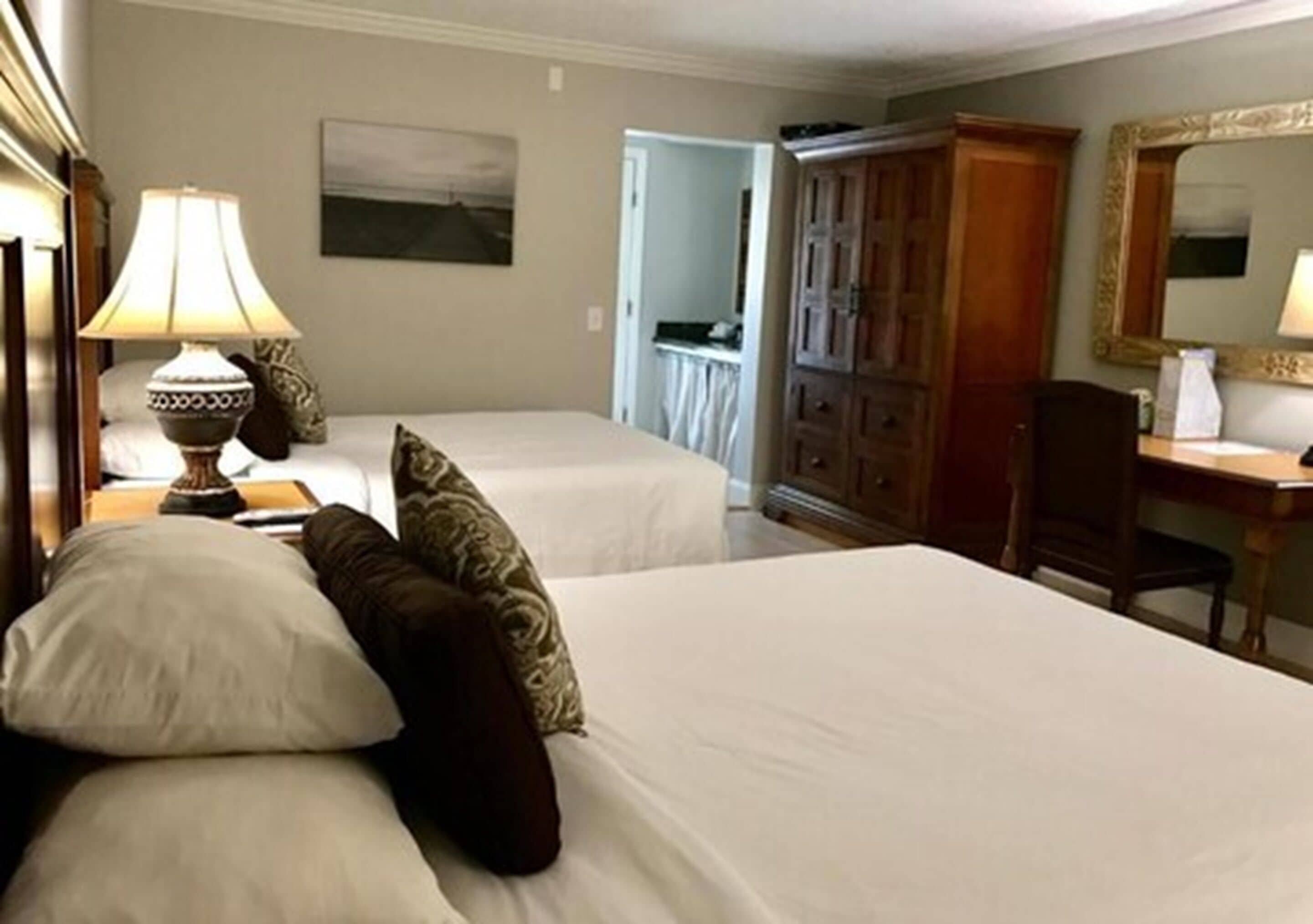 Ein Hotelzimmer mit zwei Betten, einem Schreibtisch, einer Lampe, einem Kleiderschrank und einem Spiegel.