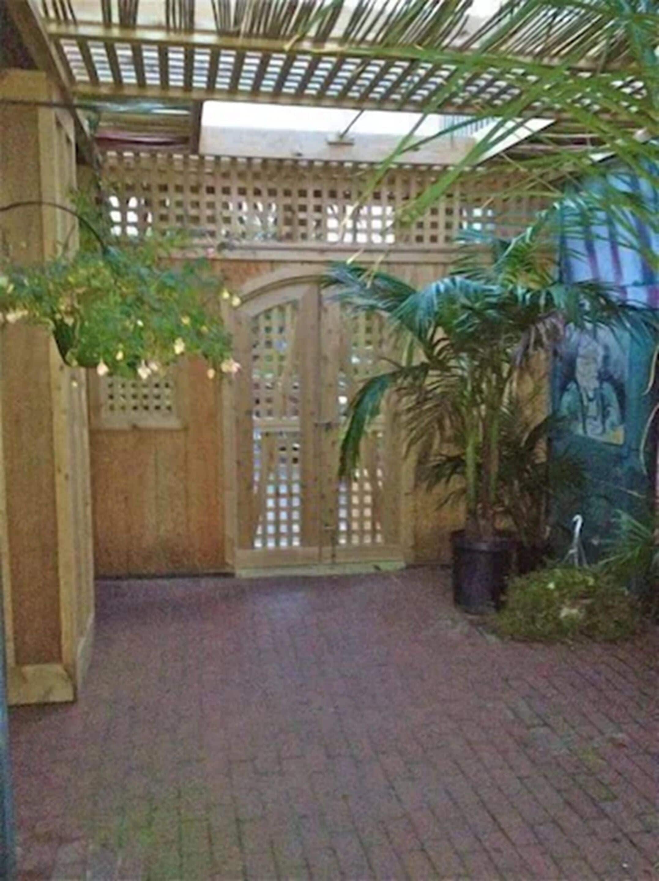 Un pasillo cubierto con una puerta de madera, plantas en macetas y piso de ladrillo.