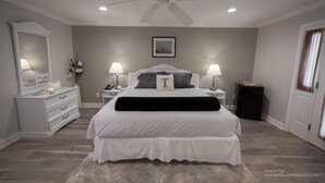 Une chambre à coucher comprenant un lit, des tables de chevet, une commode, un ventilateur de plafond et un tableau encadré accroché au mur.