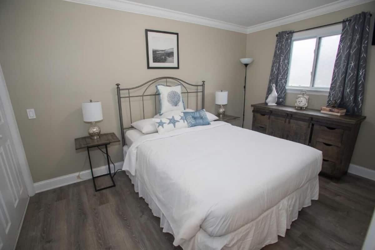 A bedroom with a bed, bedside tables, a dresser, a lamp, and a window with curtains.