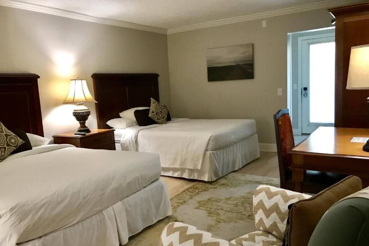 A hotel room with two beds, a desk, a chair, and a door.
