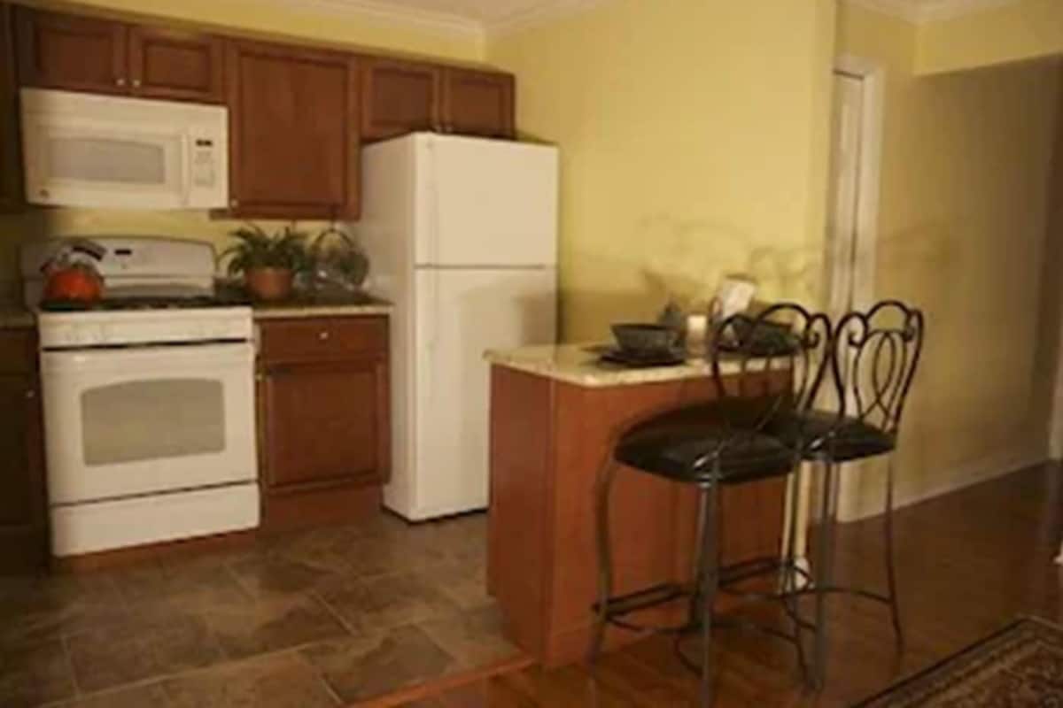 A kitchen with wooden cabinets, a white refrigerator, a stove, and a bar stool.