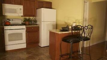Una cocina con armarios de madera, un refrigerador blanco, una estufa y un taburete de bar.