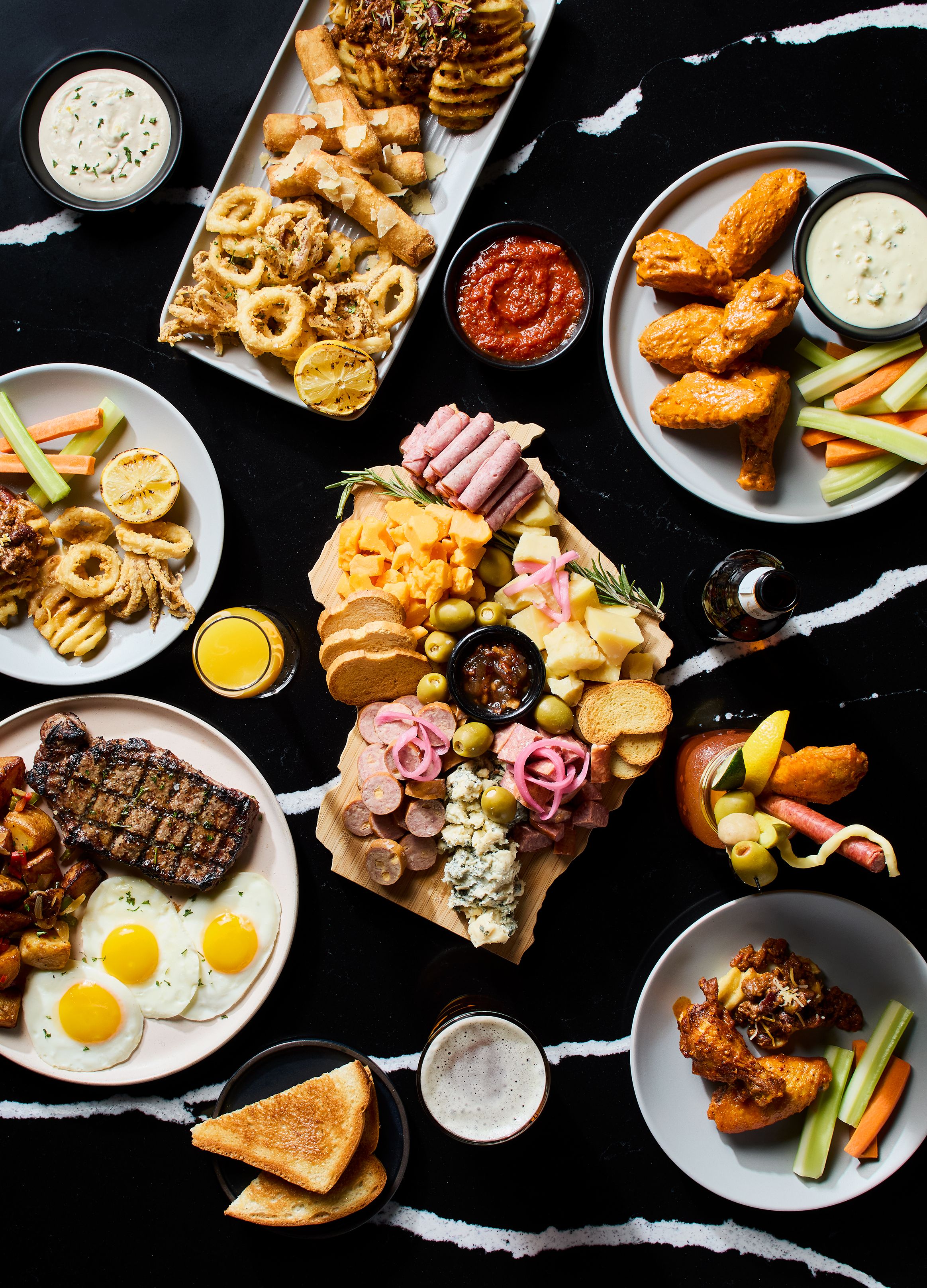 A variety of food items including grilled steak, eggs, and multiple platters of appetizers.