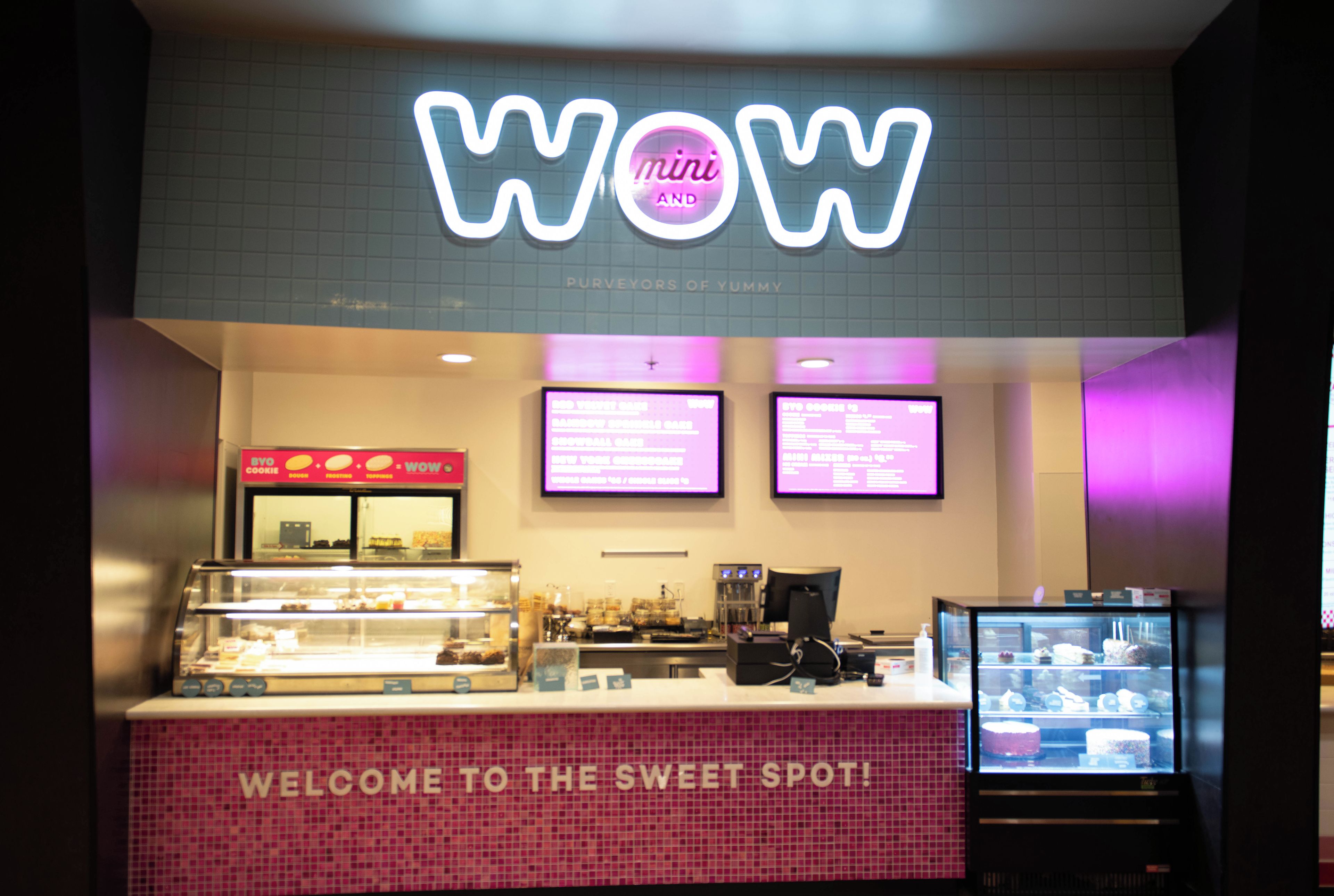 A bakery with a neon sign reading 'WOW mini AND' and a display case filled with baked goods.