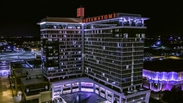A multi-story hotel with a prominent "POTAWATOMI" sign, featuring a modern architectural design with extensive glass facades and a rooftop terrace.