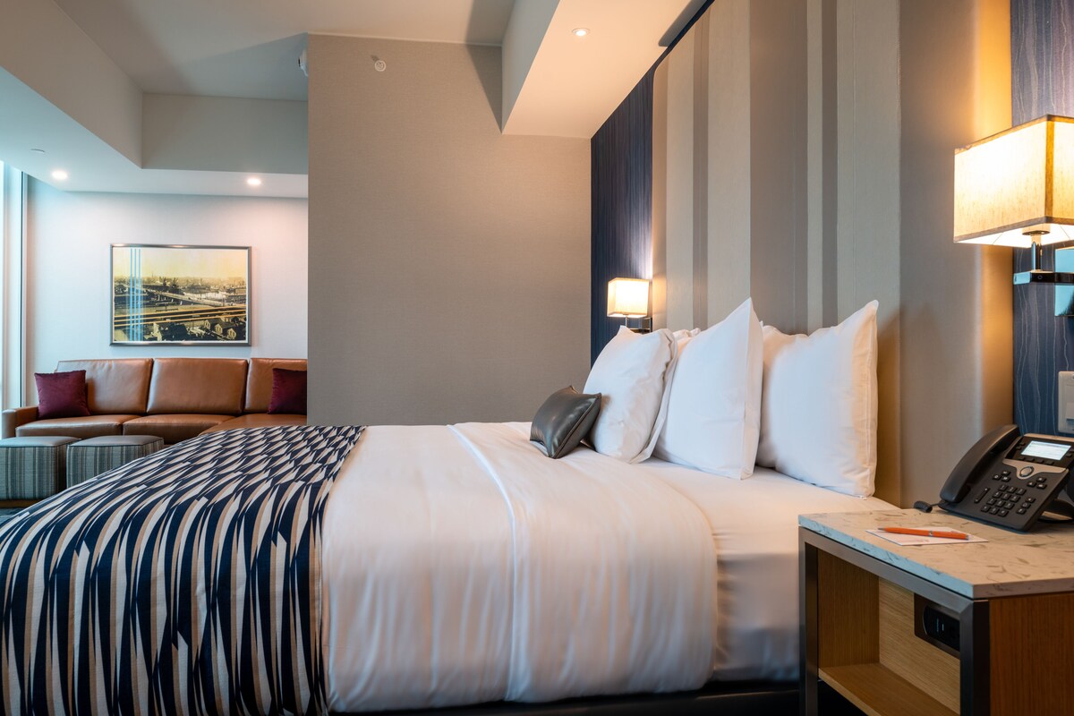A hotel room with a large bed, a desk with a phone, and a sofa with cushions.
