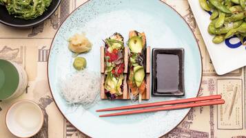 A plate with sushi, pickled vegetables, and a small dish of sauce, accompanied by chopsticks and a bowl of soup.