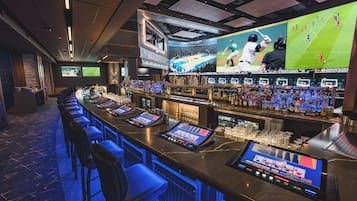 A bar area with multiple screens displaying sports events, a long counter with bar stools, and a variety of bottles and glasses.