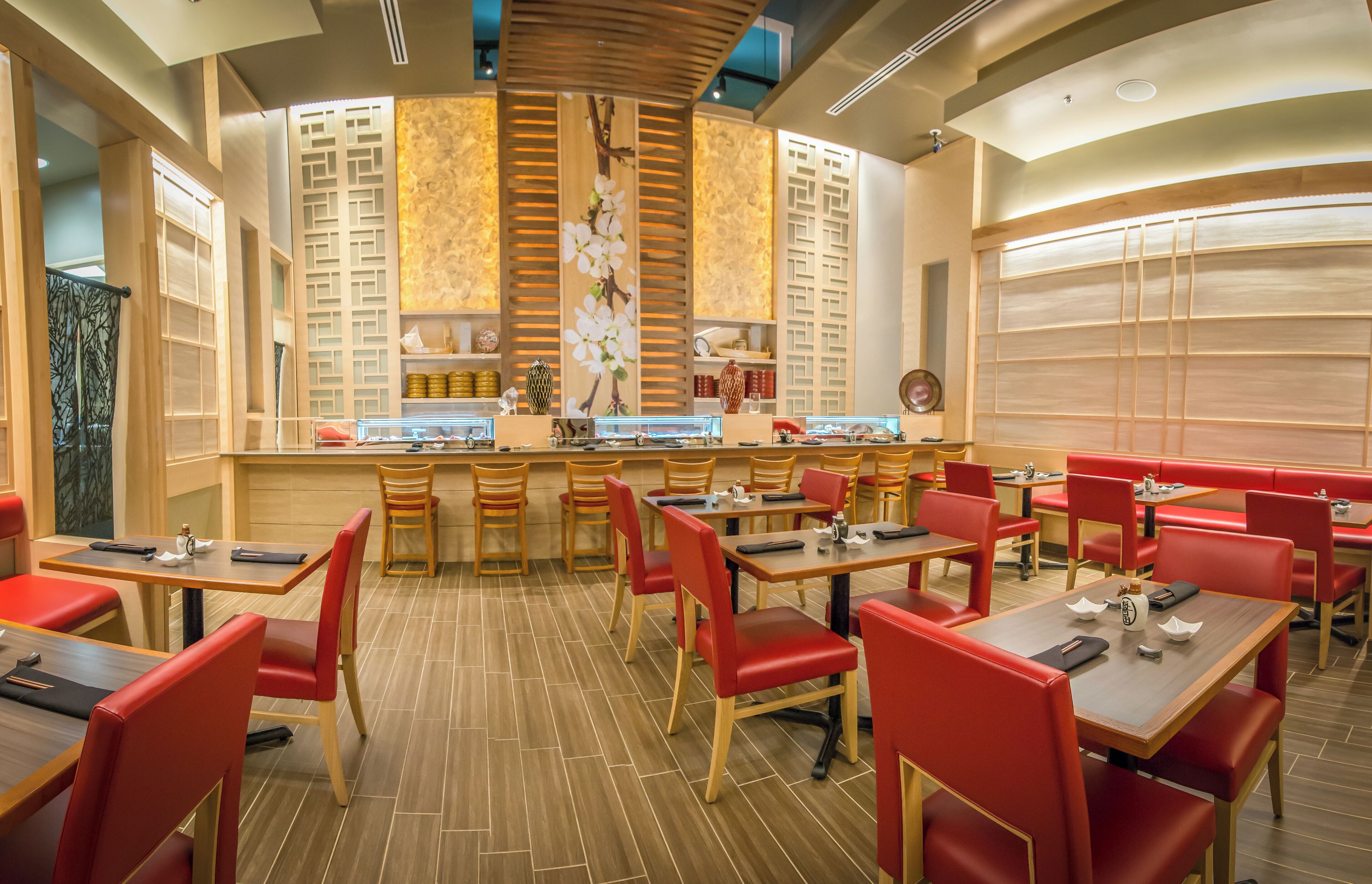 A restaurant with wooden tables and red chairs, a central bar area, and decorative wall panels.