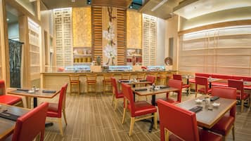 A restaurant with wooden tables and red chairs, a central bar area, and decorative wall panels.