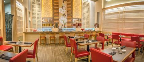 A restaurant with wooden tables and red chairs, a central bar area, and decorative wall panels.