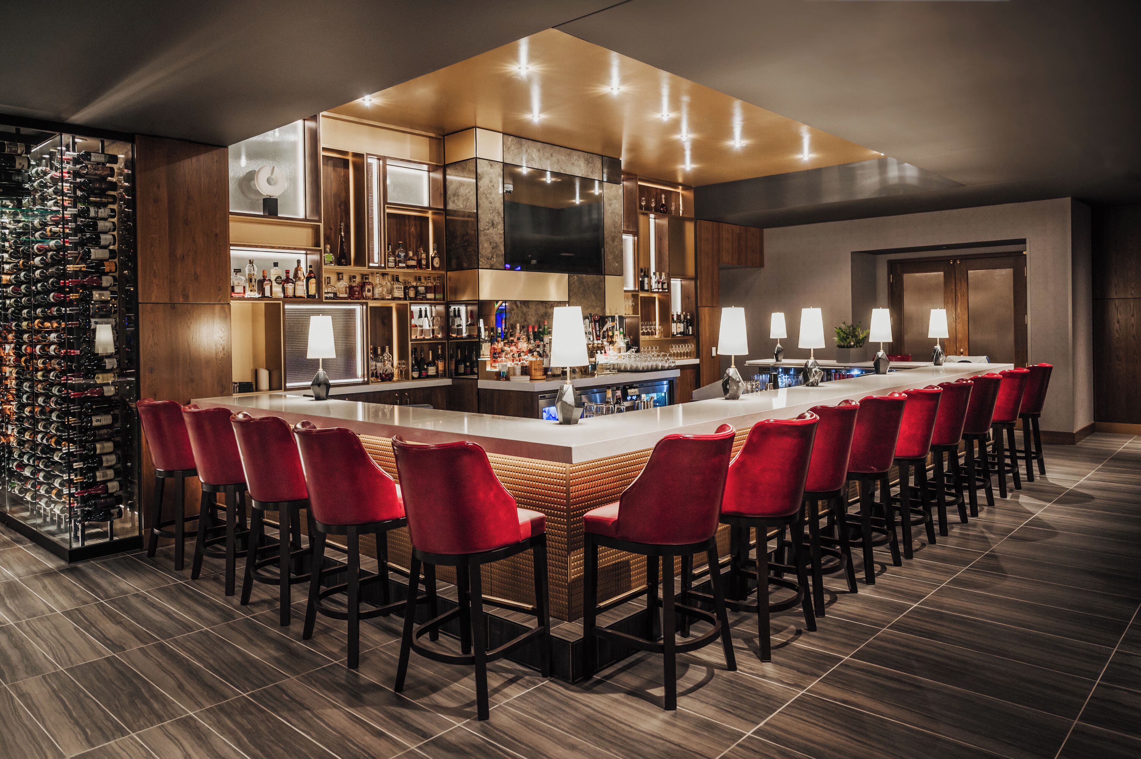 A bar area with a long counter, red bar stools, and a wine rack.