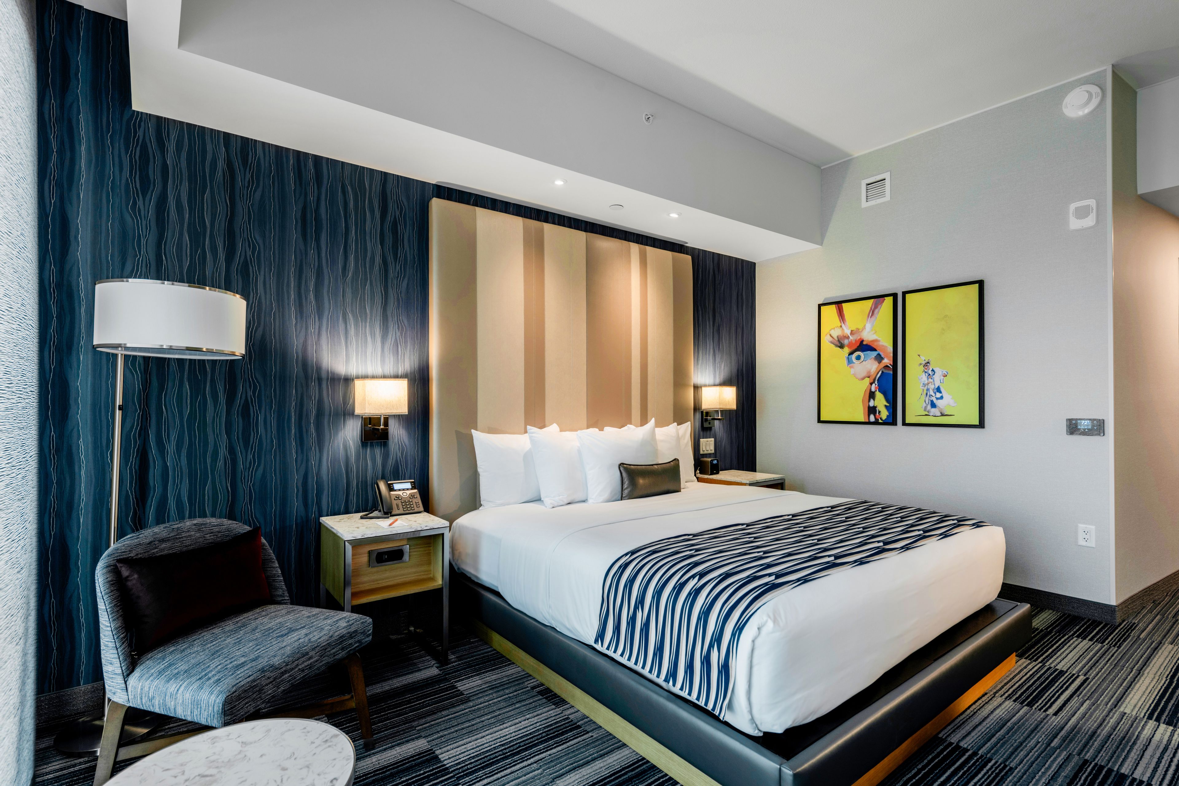 Una habitación de hotel moderna con una cama grande, un escritorio, una silla y dos lámparas fijadas a la pared.