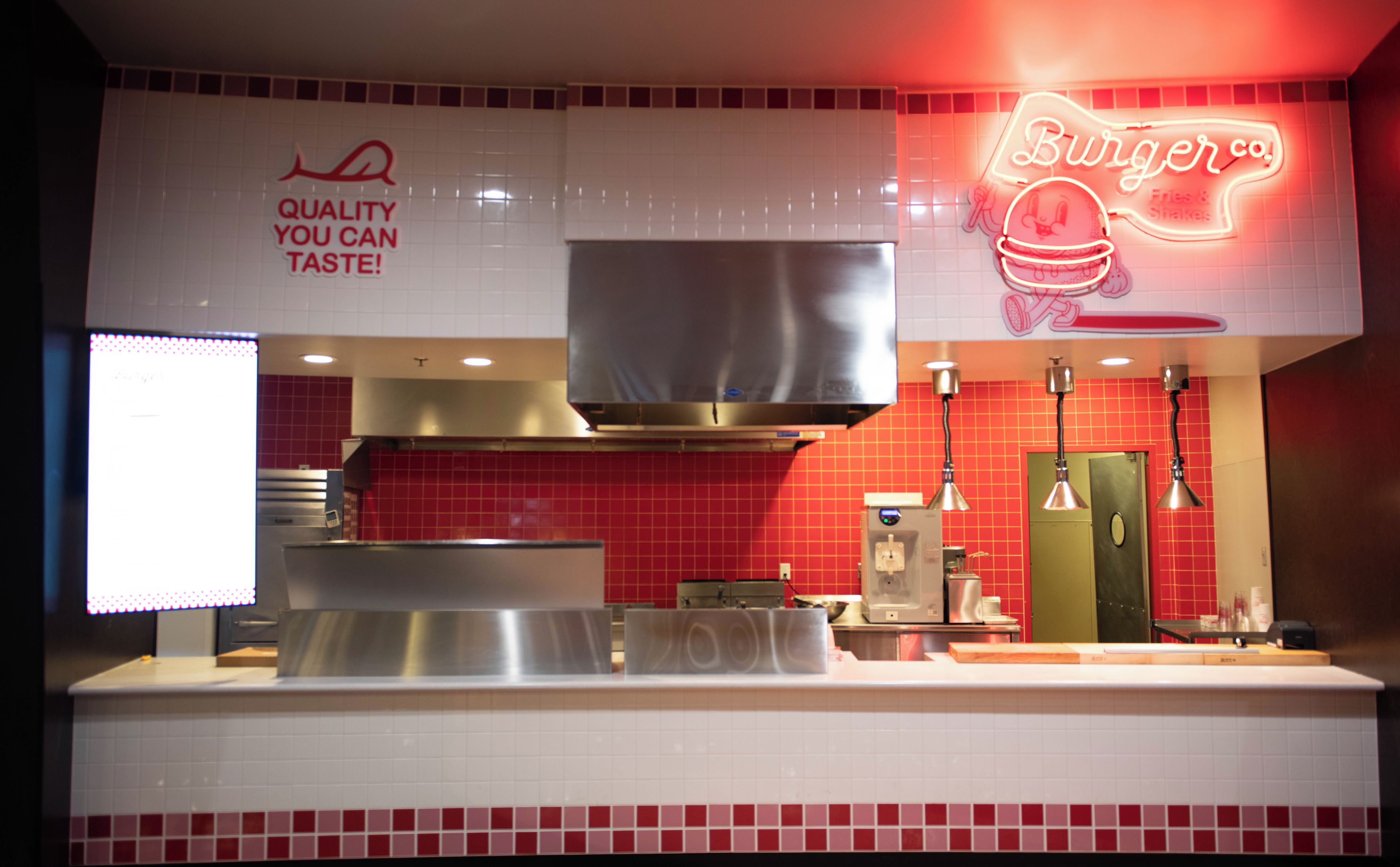 A kitchen with red tiles, a neon sign for Burger Co., and a stainless steel range hood.