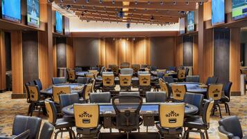 A conference room with multiple tables and chairs, wooden paneling on the walls, and ceiling-mounted screens.