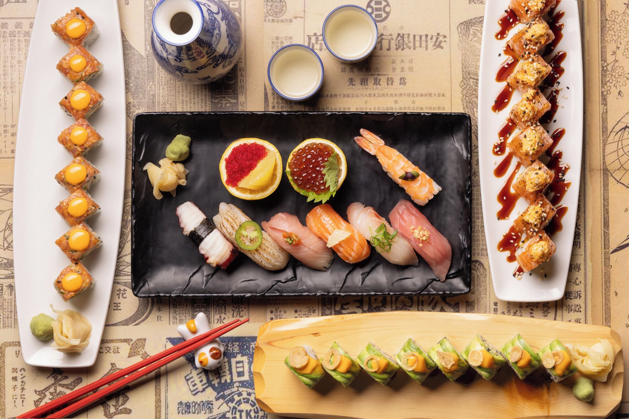 A variety of sushi dishes on different plates, including nigiri, sashimi, and rolls, with chopsticks and small bowls of soy sauce and wasabi.