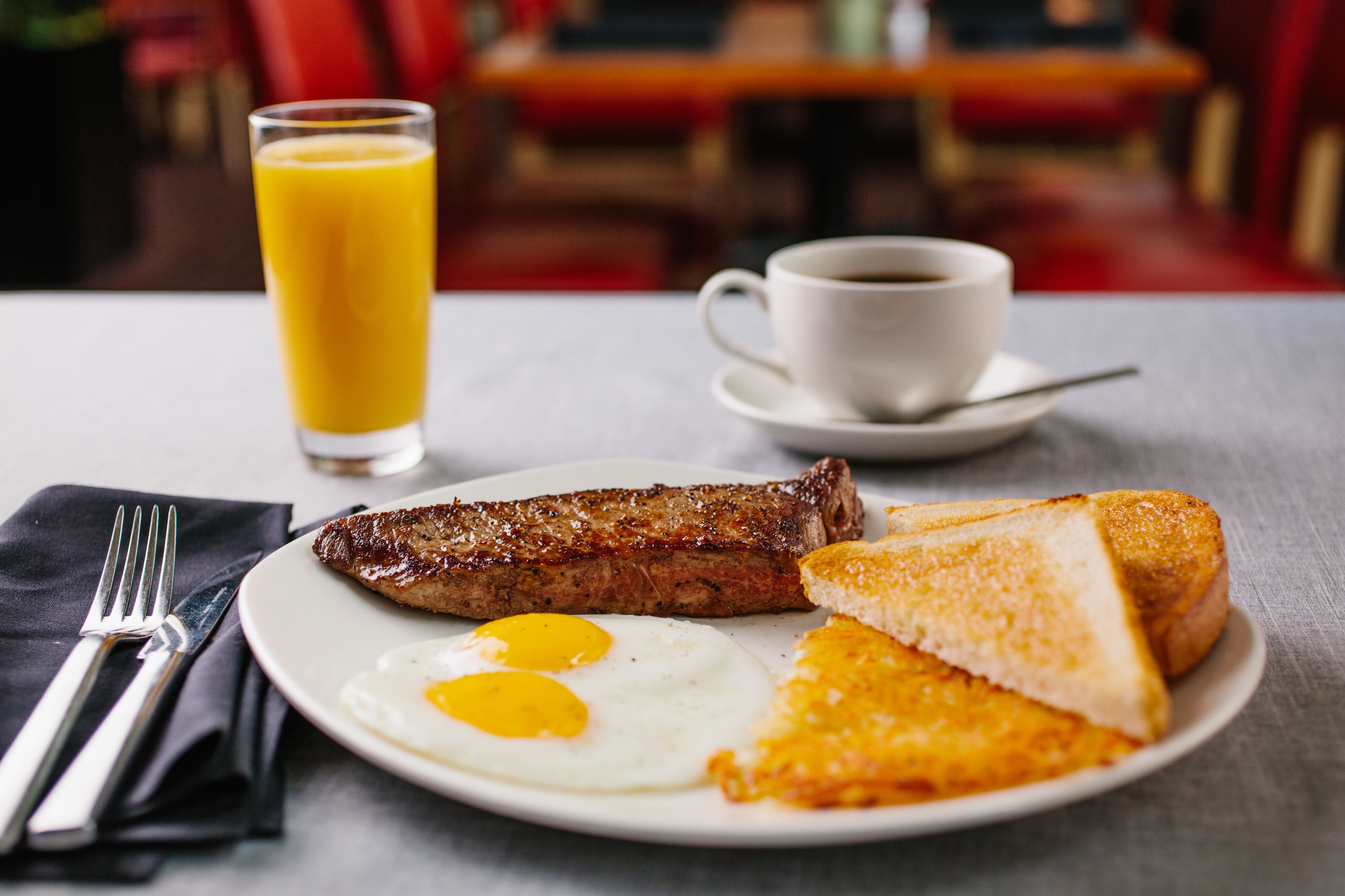 A breakfast plate with eggs, toast, and sausage, a glass of orange juice, and a cup of coffee on a table.