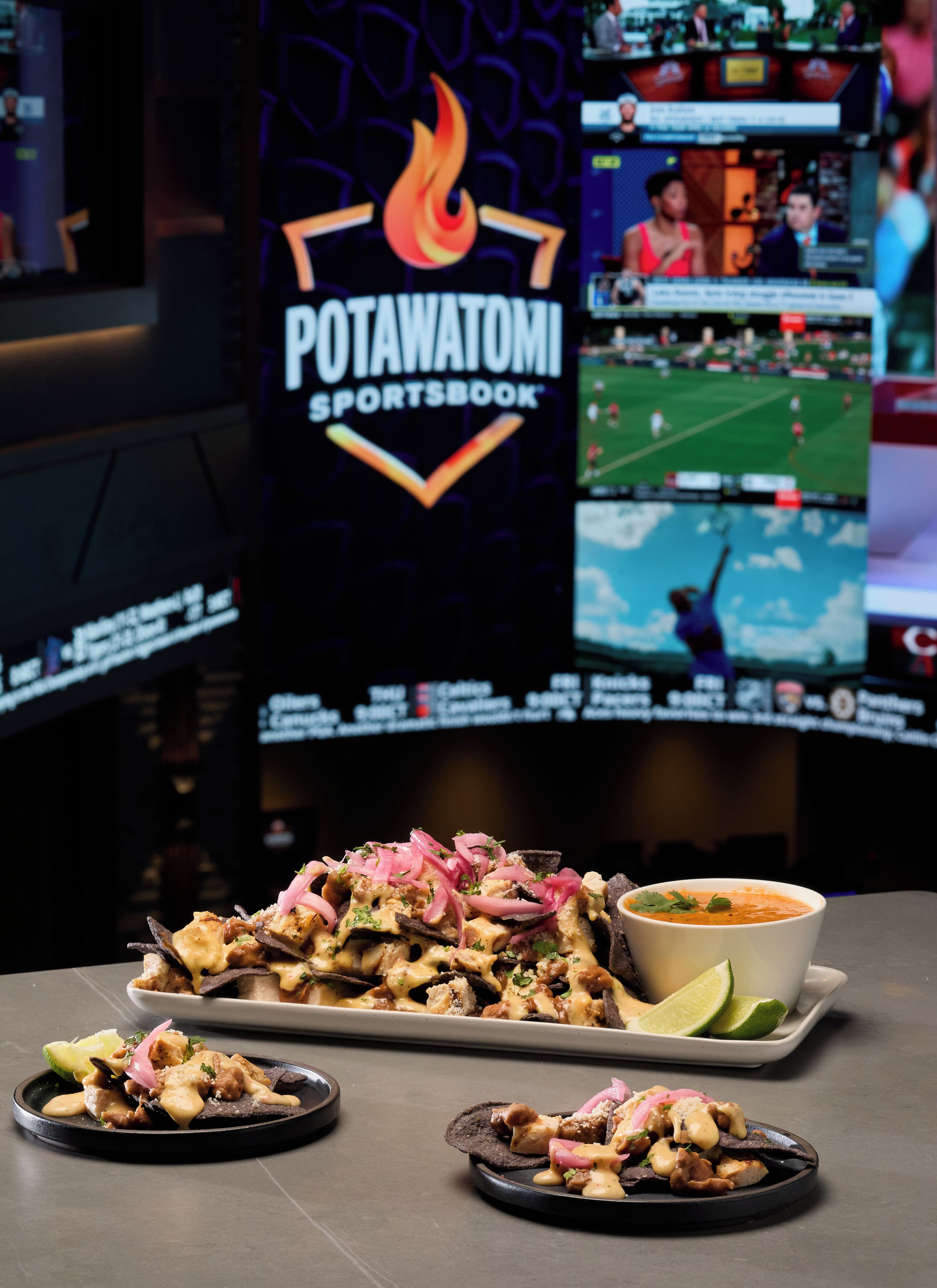 Un restaurante de temática deportiva con una pantalla grande mostrando un partido de fútbol, una porción de nachos y un tazón de sopa.