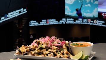 Un restaurante de temática deportiva con una pantalla grande mostrando un partido de fútbol, una porción de nachos y un tazón de sopa.