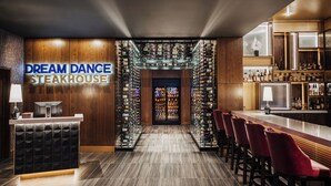 A bar area with a wooden reception desk, a wine rack, and red bar stools.