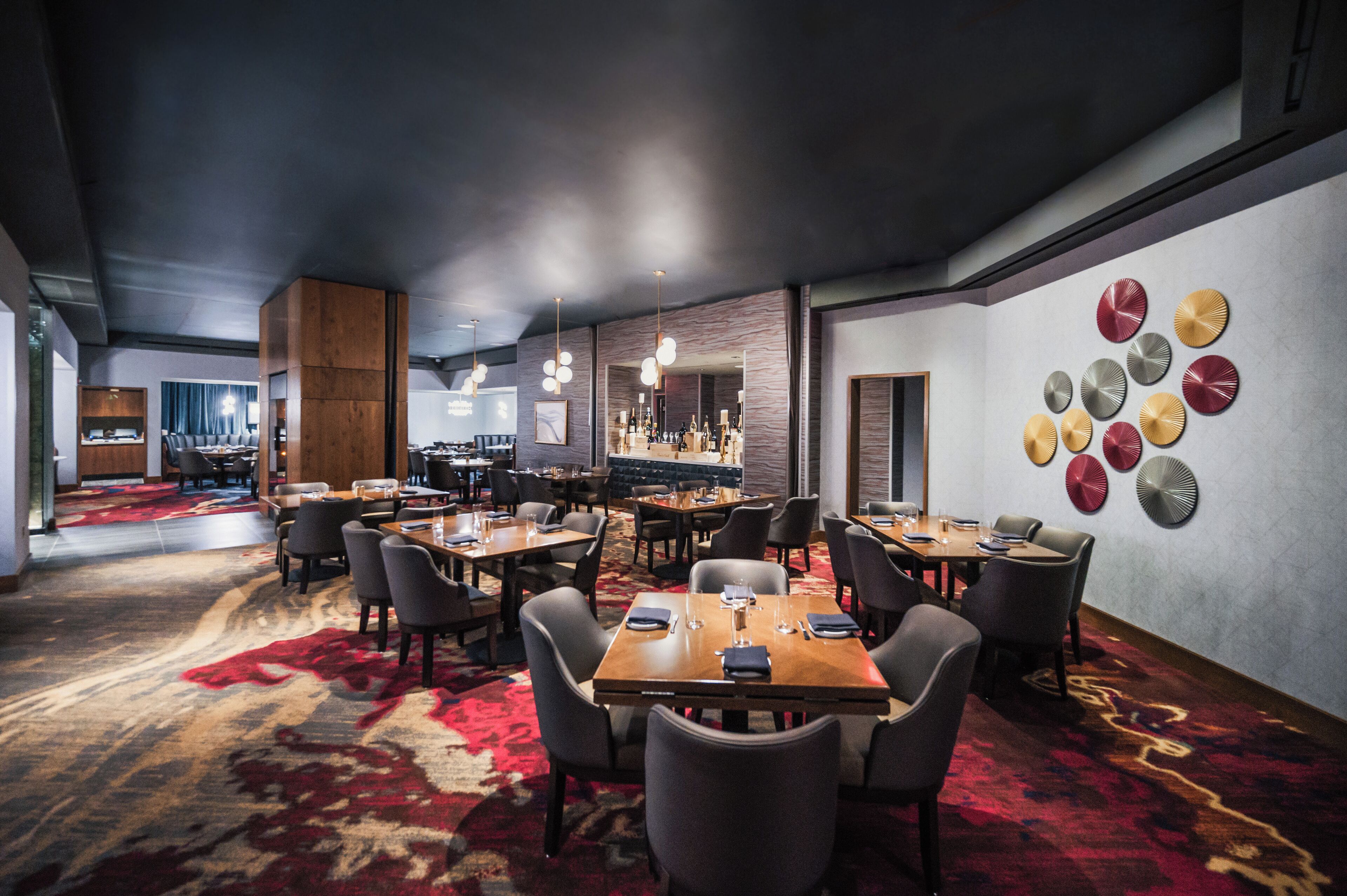 A hotel lobby with multiple dining tables and chairs, a bar area, and a wall with decorative plates.