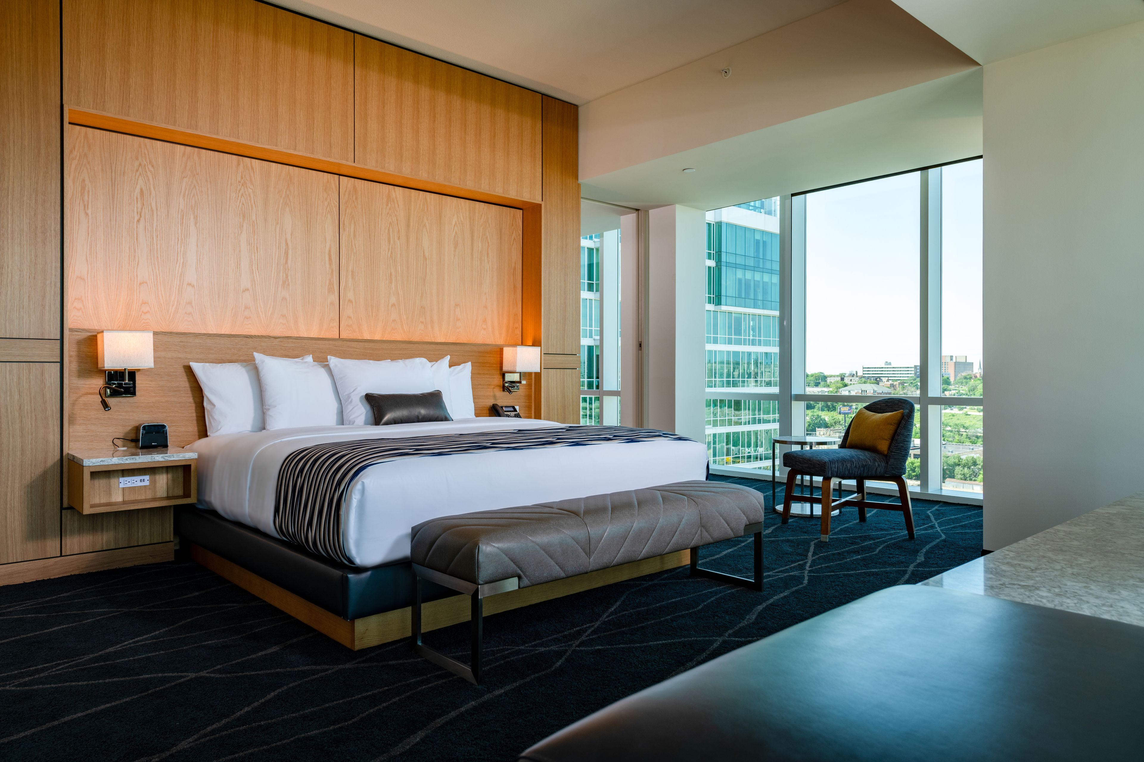 A modern hotel room with a large bed, a bench, a desk, and a chair.