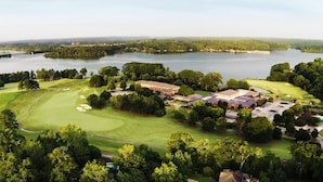 Campo de golf con club house, rodeado de árboles densos y una gran masa de agua.