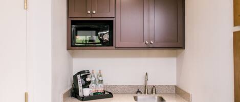 A compact kitchen with a built-in microwave, a coffee maker, and a sink.