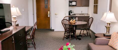 A compact hotel room with a dining area, kitchenette, and a living space.